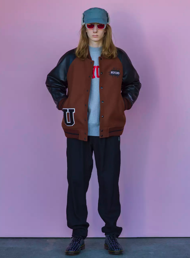 A man wearing an Undercover outfit featuring a coaches jacket, sweatshirt, black pants and snakeskin boots