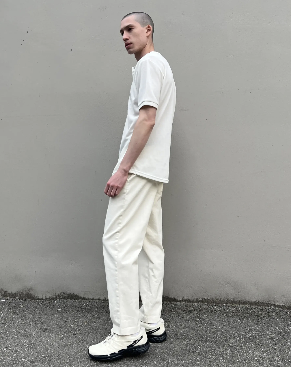 A man standing outside wearing a Oak + Fort all-white and cream outfit with salomon shoes