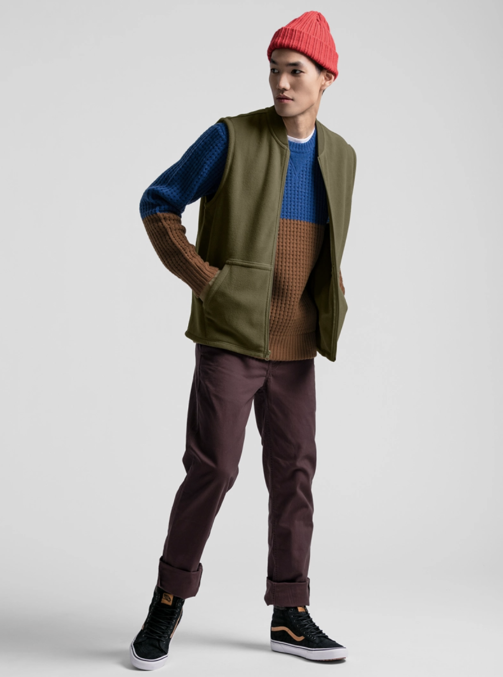 A man wearing a JackThreads outfit featuring a red beanie. green vest and red pants