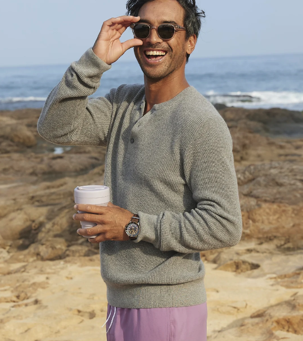 A man at the beach wearing an Outerknown outfit featuring a grey long-sleeve and shorts