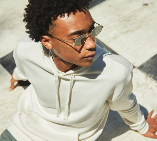 A man sitting looking away wearing a Alternative Apparel cream hoodie with sunglasses