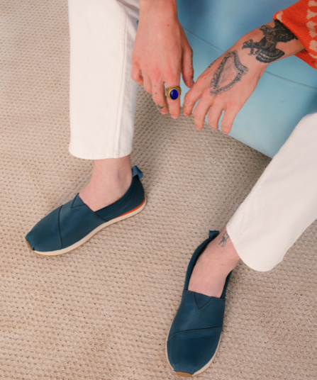 A man sitting wearing navy blue slip-on Tom's shoes