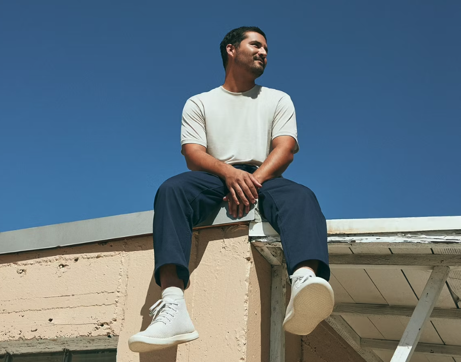 A man sitting on a roof in an Allbirds outfit featuring grey shoes