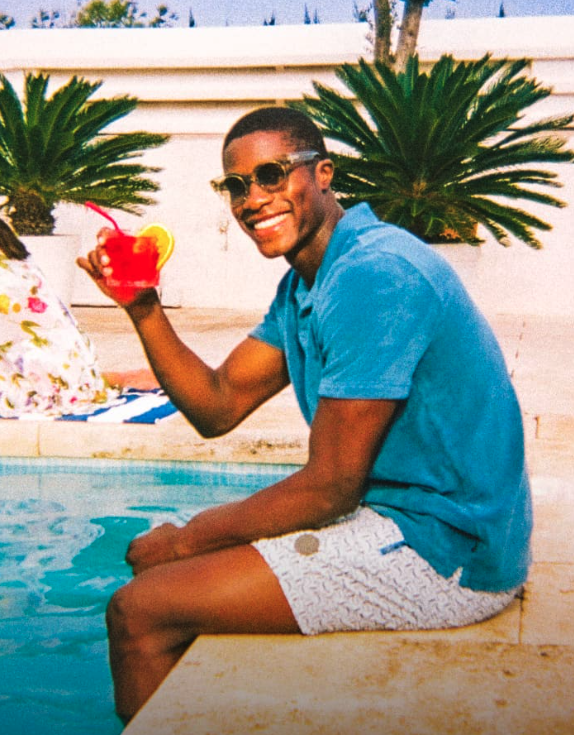 A man sitting by a pool in Ted Baker swimshorts and a blue polo