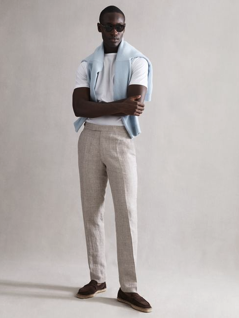 A man wearing a modern country club outfit by Reiss with a baby blue sweater draped across his shoulders