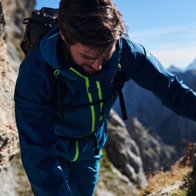 A man hiking in a blue and green Jack Wolfskin jacket and pants