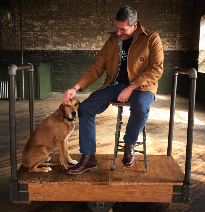 A man sitting with a dog wearing a LC King outfit featuring modern workwear