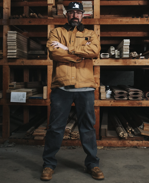 A man wearing a Wolverine brown jacket with his arms crossed
