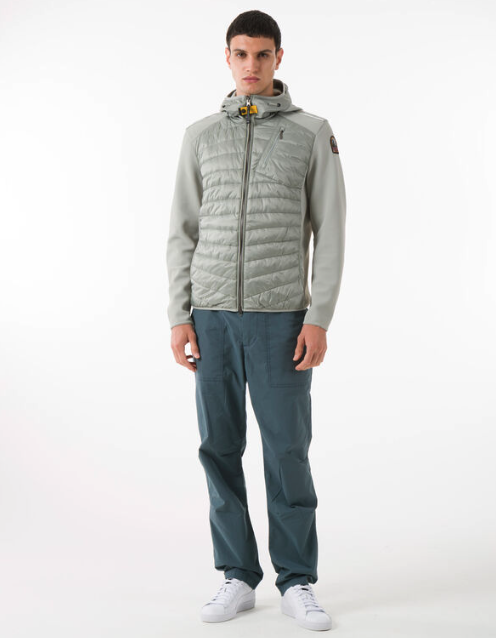 A man wearing a light grey Parajumpers puffy jacket along with blue pants and white shoes