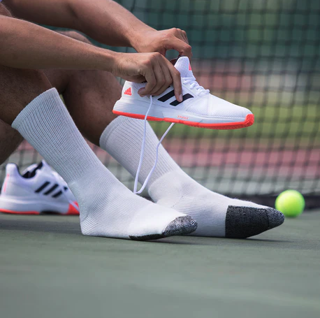 A man putting on tennis shoes wearing white Thorlo Socks