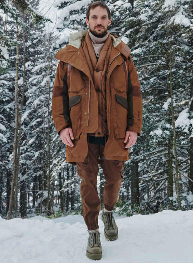 A man wearing a layered brown White Mountaineering outfit with two brown jackets and matching brown pants