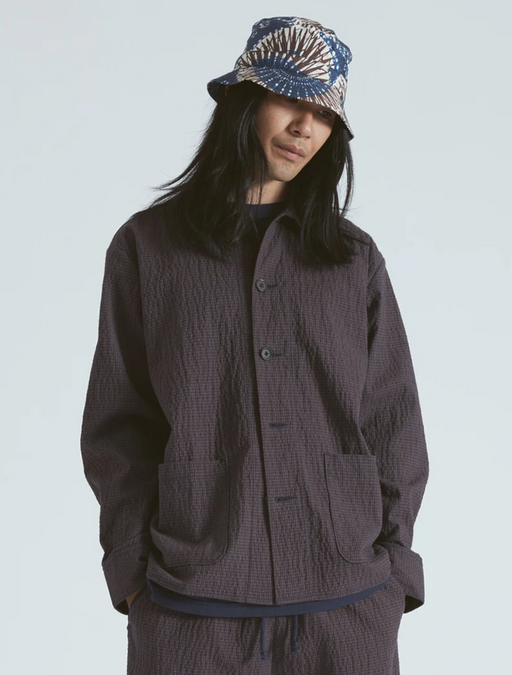 A man wearing a full Universal Works dark outfit with a graphic button up