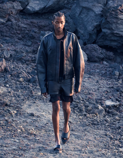 A man wearing a futuristic all-black Alyx outfit walking on the beach