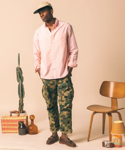 A man wearing a Gitman Vintage outfit featuring a pink button up shirt and camo pants