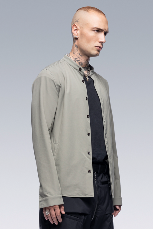A man wearing a sleek Acronym outfit featuring a olive button up with a black shirt underneath