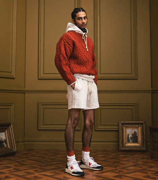 A man wearing a New Balance outfit featuring a red sweater and white shorts