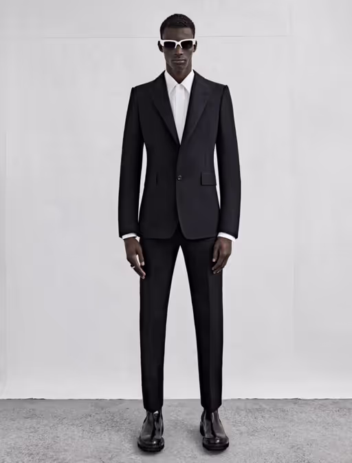 A man wearing a black Alexander McQueen suit with black and white sunglasses