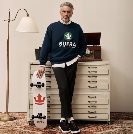 A man wearing a Supra crewneck sweater with a white button shirt underneath