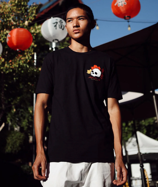 A man wearing a Riot Society skull t-shirt in black with white pants