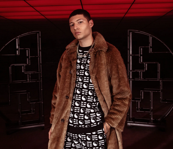 A man wearing a clot fur coat and branded yin and yang all over print shirt