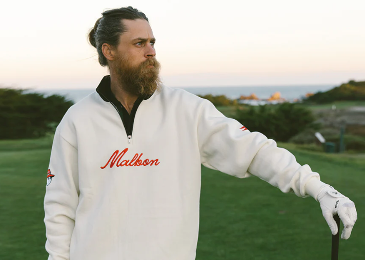 A man wearing a white Malbon golf sweater and golf glove