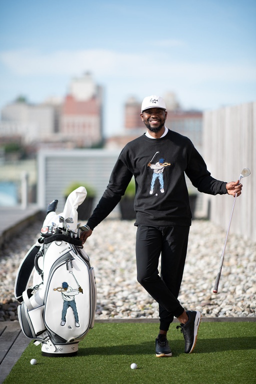 A man golfing wearing a Eastside Golf outfit featuring a sweater and hat