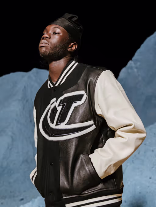 A man wearing a coaches varsity jacket by Trapstar