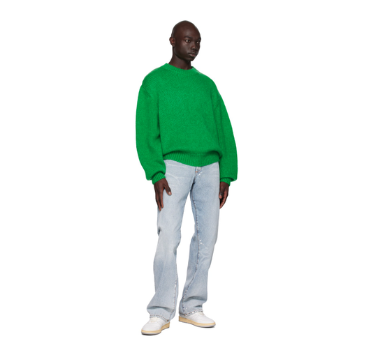 A man wearing a green Represent sweater with blue jeans