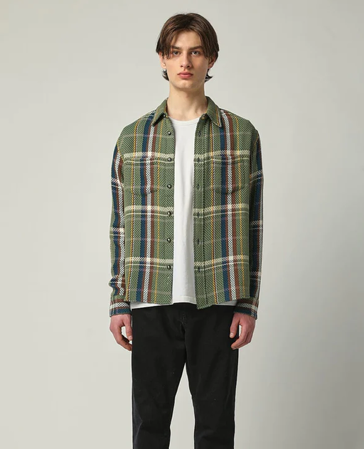 A man wearing a green flannel Corridor jacket with a white t-shirt beneath it