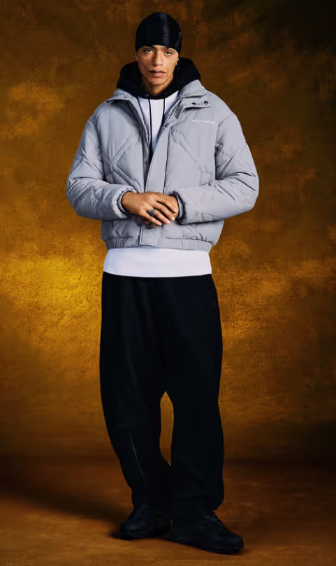 A man wearing a Daily Paper outfit with a grey jacket and white shirt