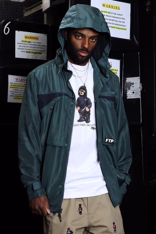 A man wearing a FTP outfit featuring a white t-shirt and blue rain coat