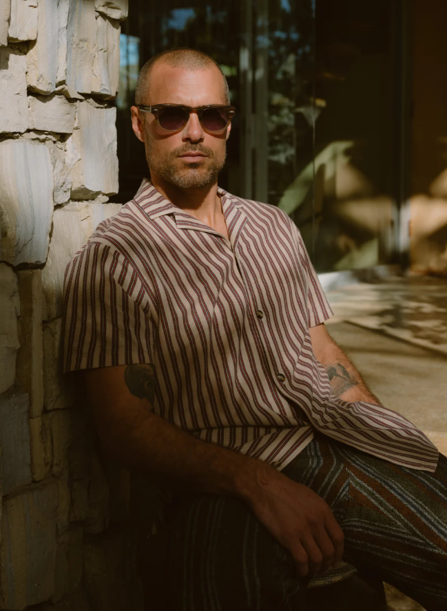 A man wearing a Barton Perreira striped shirt in red and white along with sunglasses