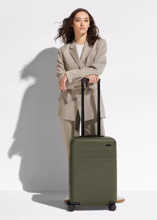 A woman holding an olive green Away suitcase