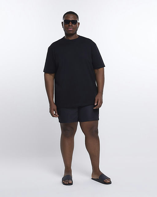 A man wearing a River Island Plus black t-shirt with black swim trunks