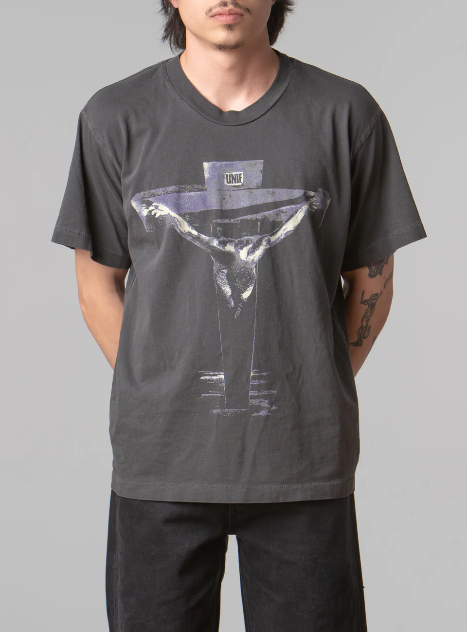 A man wearing a black UNIF t-shirt featuring a cross with black pants