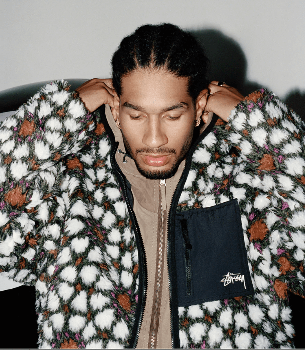 A man wearing a white and brown Stussy fleece with a brown jacket underneath