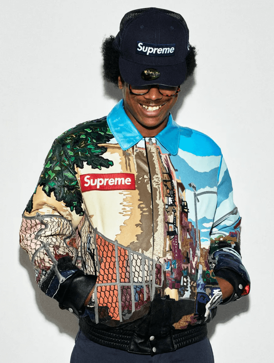 A man wearing a Supreme NYC style colorful graphic coaches jacket with a supreme box logo hat