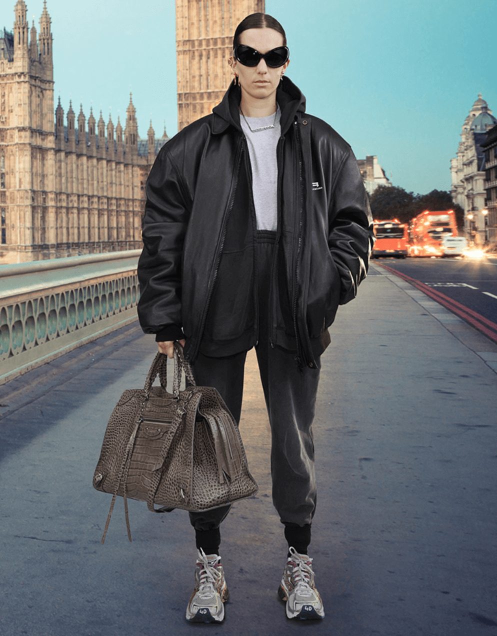 A person wearing a Balenciaga black leather sports coat, dark grey sweats, white sneakers and oversize sunglasses