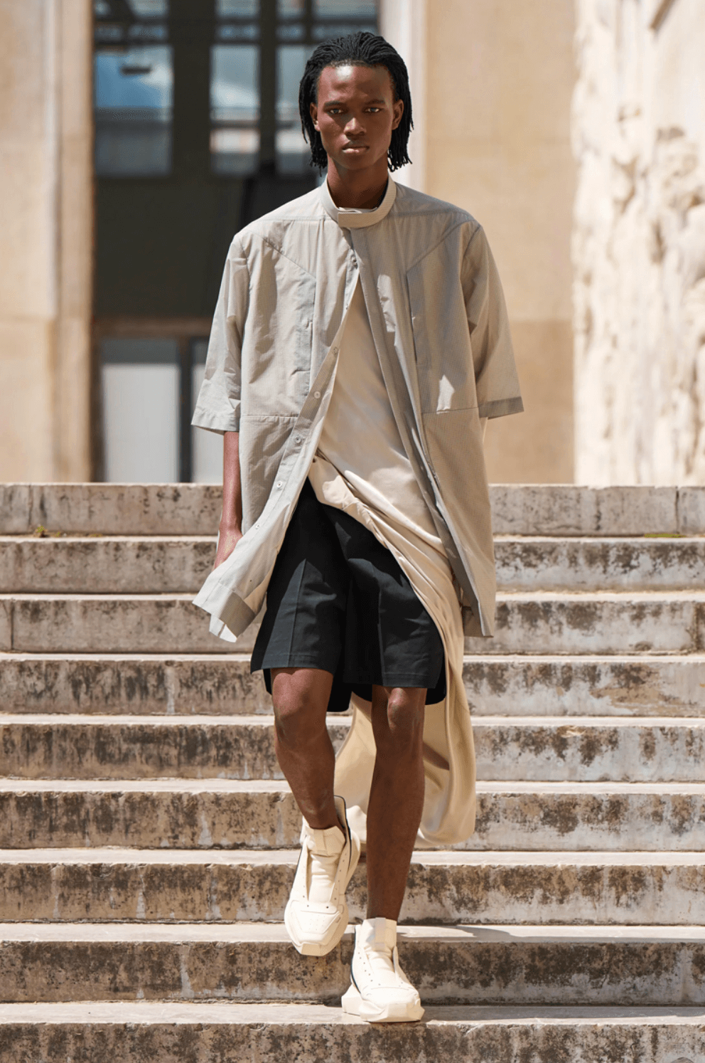 A man walking down steps on a sunny day wearing a Rick Owens outfit featuring a space grey overshirt, black shorts and shoes