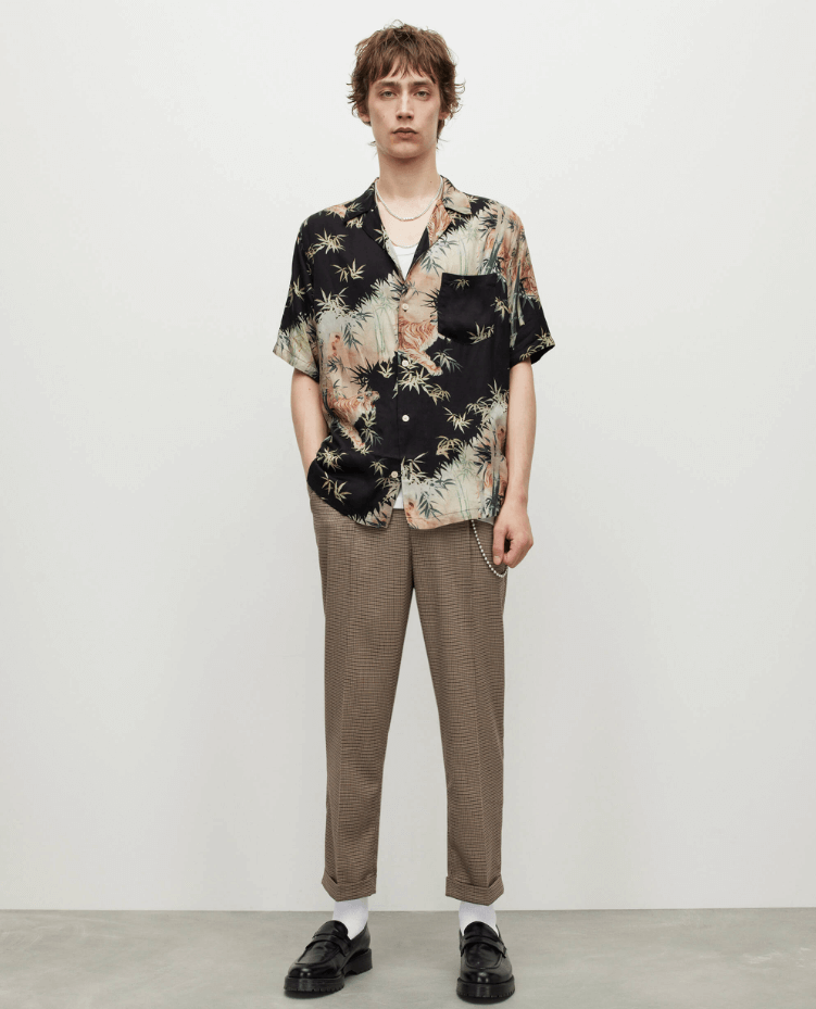 A man standing wearing an AllSaints dark floral short-sleeve button up with beige pants