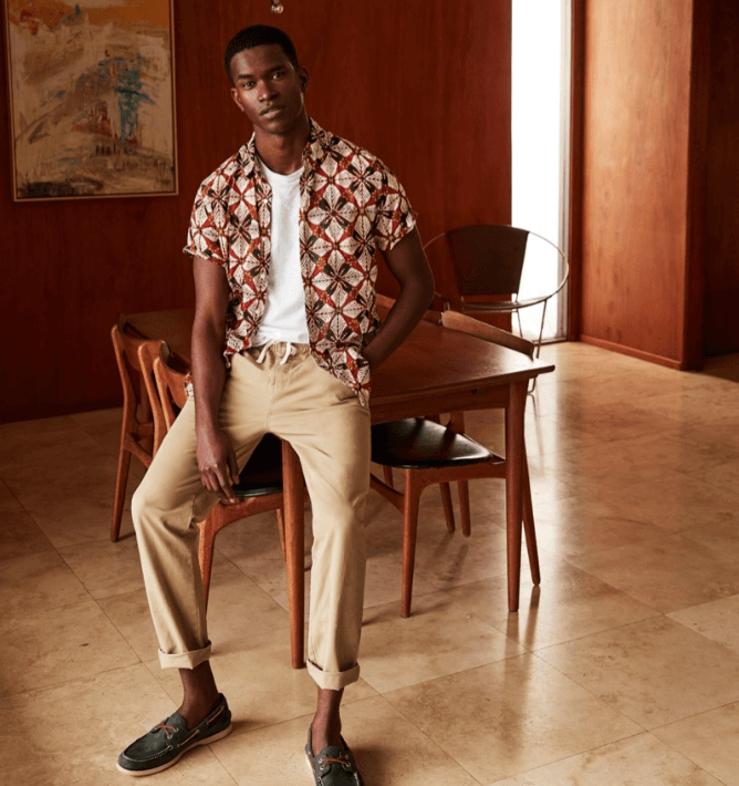 A man wearing a patterned J Crew short-sleeve button up with rolled up beige khakis and boat shoes