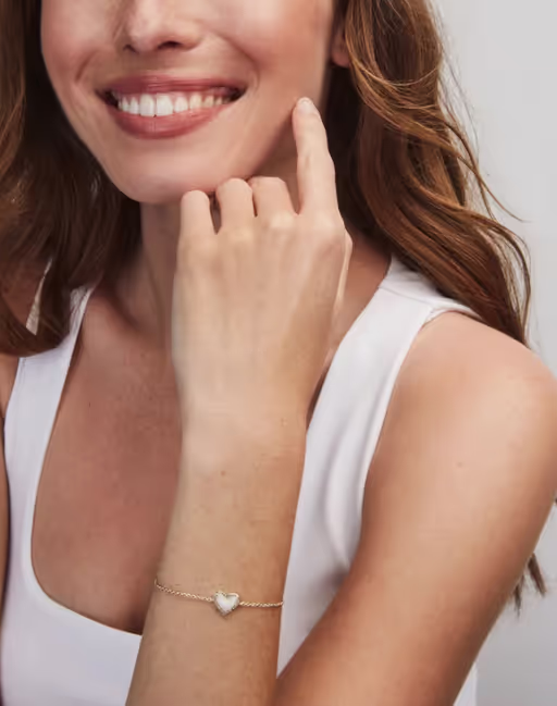 A woman wearing Kendra Scott ari heart gold delicate chain bracelet in bubblegum pink