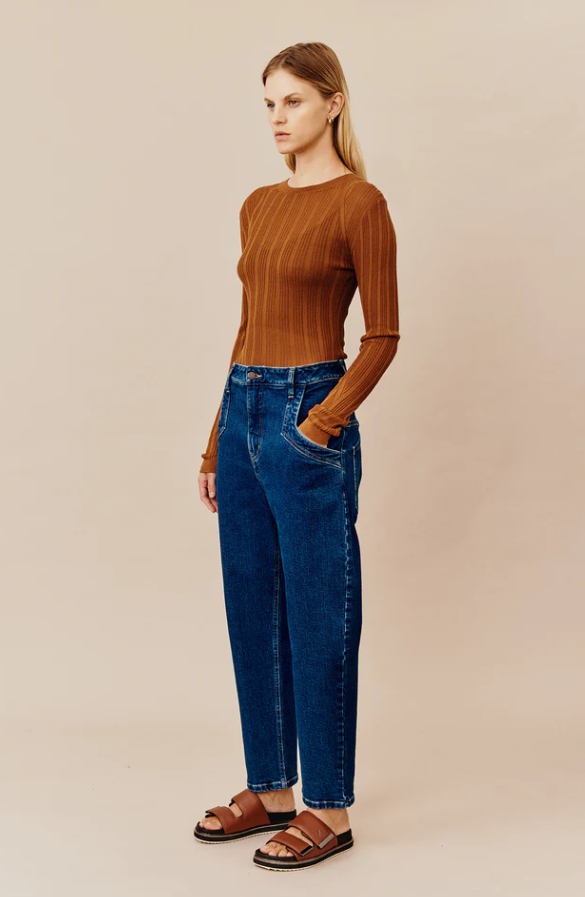A woman wearing a dark orange Ginger and Smart shirt with blue jeans