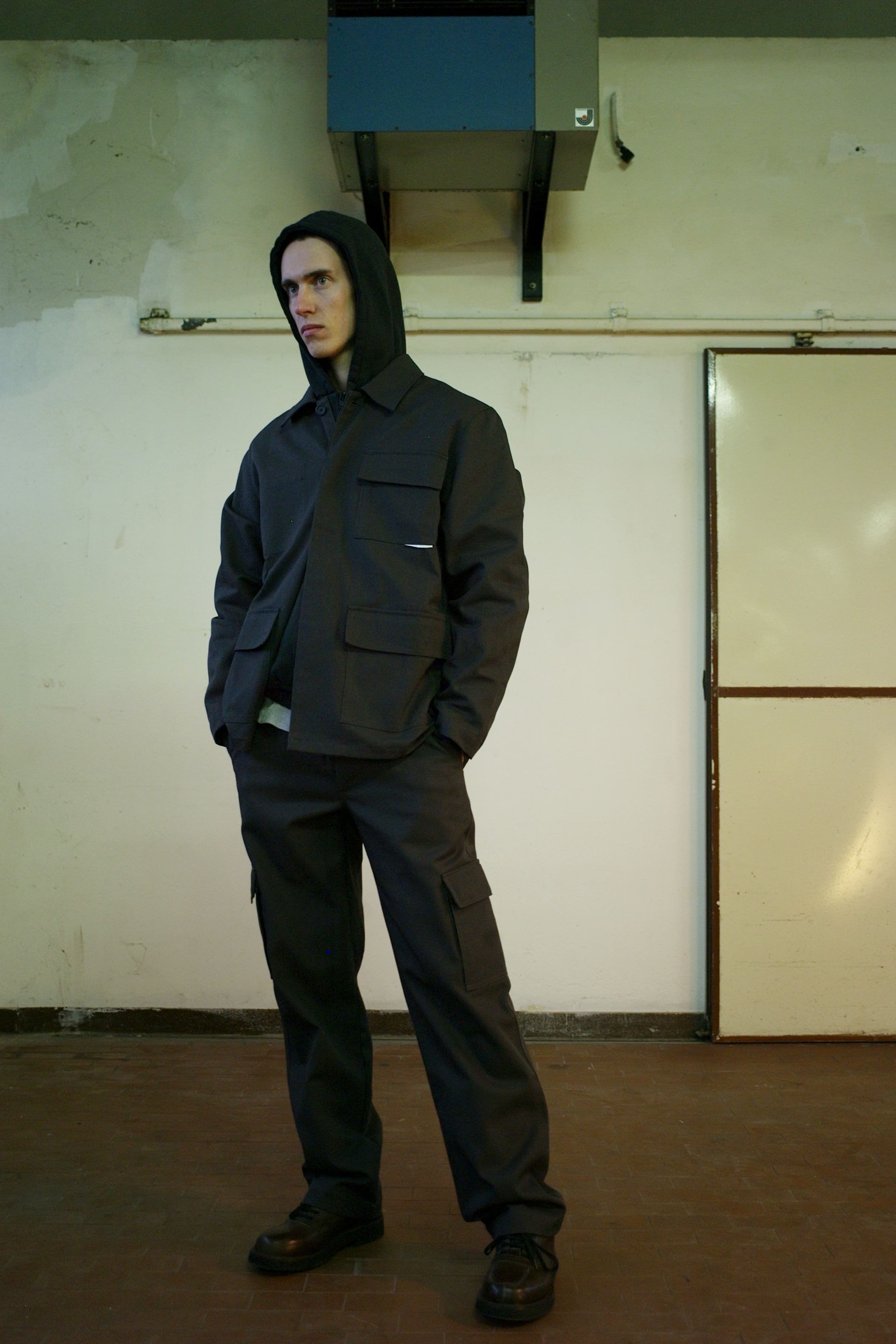 A man wearing a dark hooded GR10K utility jacket with cargo trousers