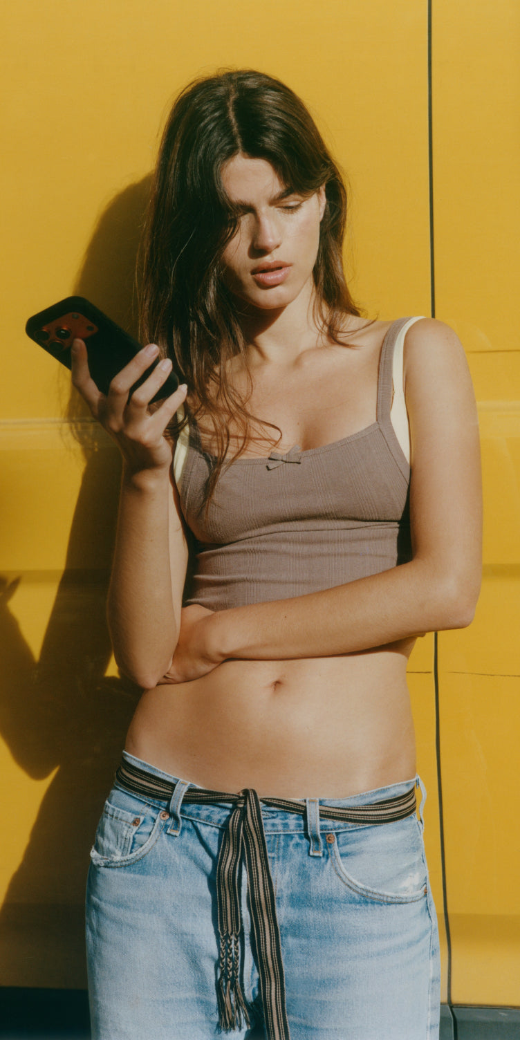Organic Basics model in a ribbed brown bra top against a yellow wall