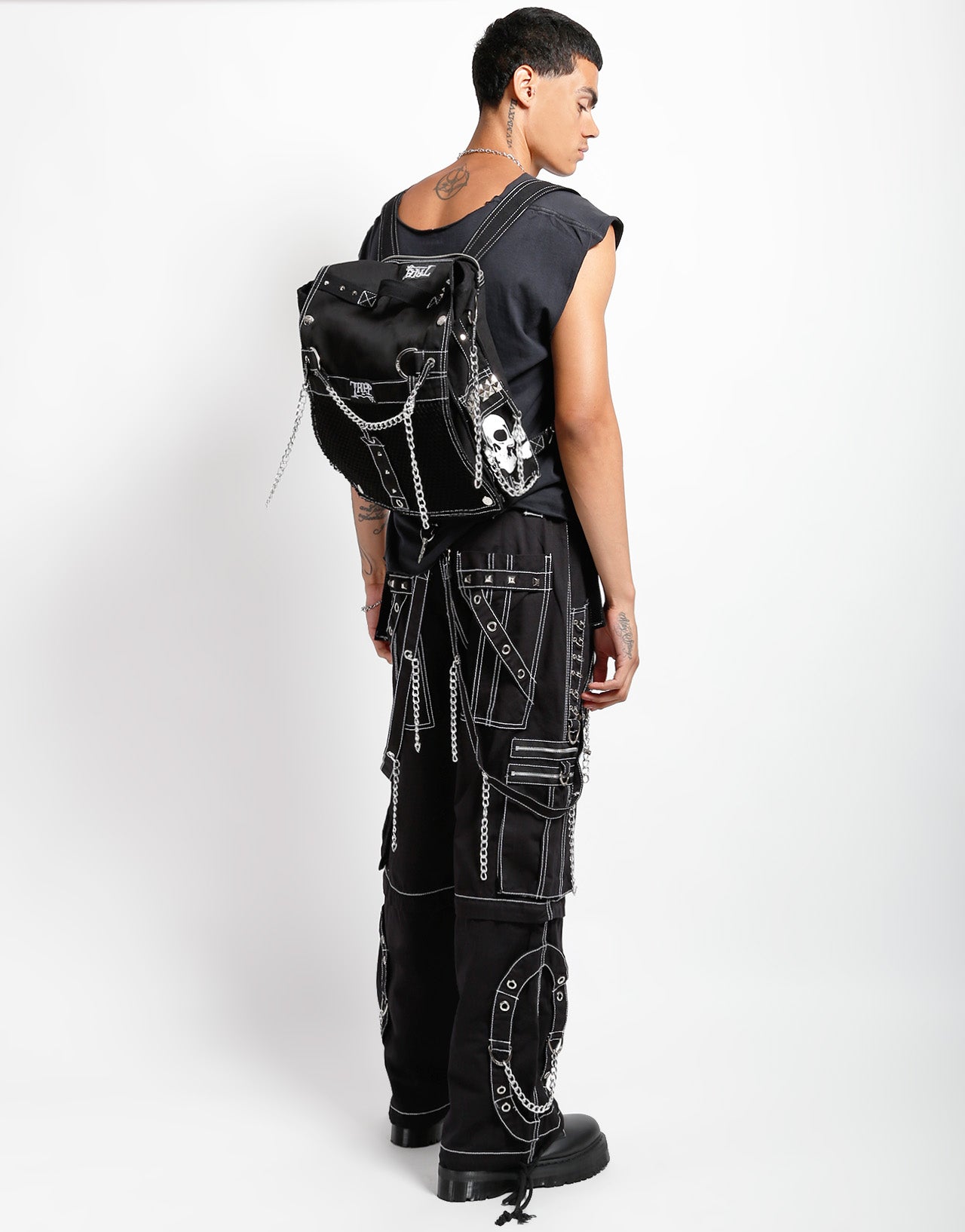 Tripp NYC model in black chained cargo pants with a studded skull backpack