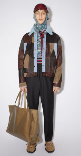 A man wearing an all over printed Acne Studios jacket with a colorful sweater underneath along with a scarf and brown bag