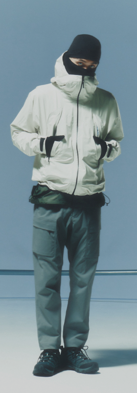 A man waring a white Goldwin jacket, grey pants and a black beanie along with black shoes and gloves