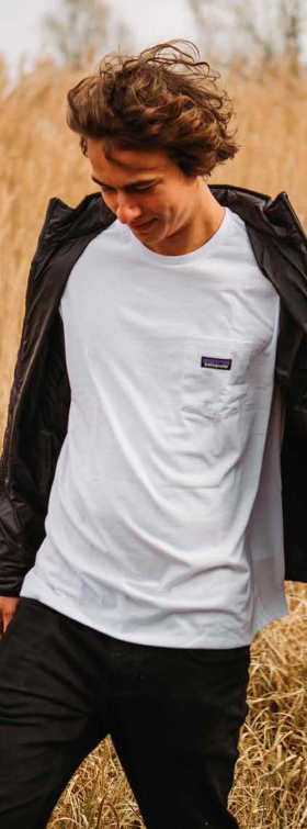 A man in a wheat field wearing a white Patagonia t-shirt along with black jacket and pants