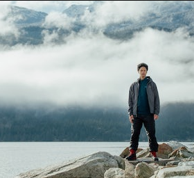 A man standing on rocks just off a lake wearing a Arc-teryx jacket, hoodie and pants